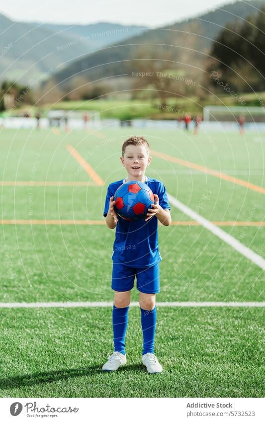 Young soccer player holding a ball on field boy football uniform sport pitch youth child sporty athletic active outdoor smiling confidence grass green blue