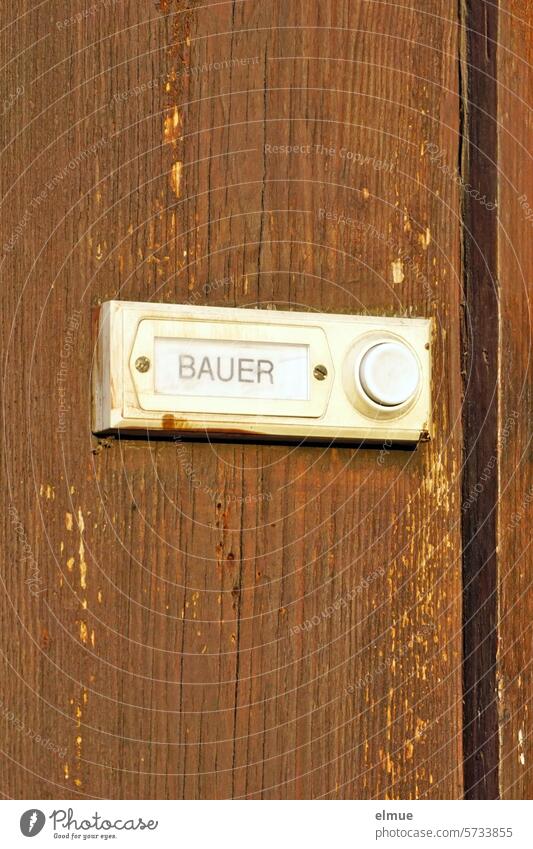 Doorbell knob with BAUER nameplate on a brown wooden wall peasant bell button Name plate dwell address farmer protests family name Signs and labeling