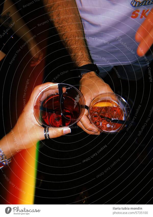 two people holding glasses with drinks at a party hands colors red spritz campari italy italian happyhour night festa led lights fun dark friends couple