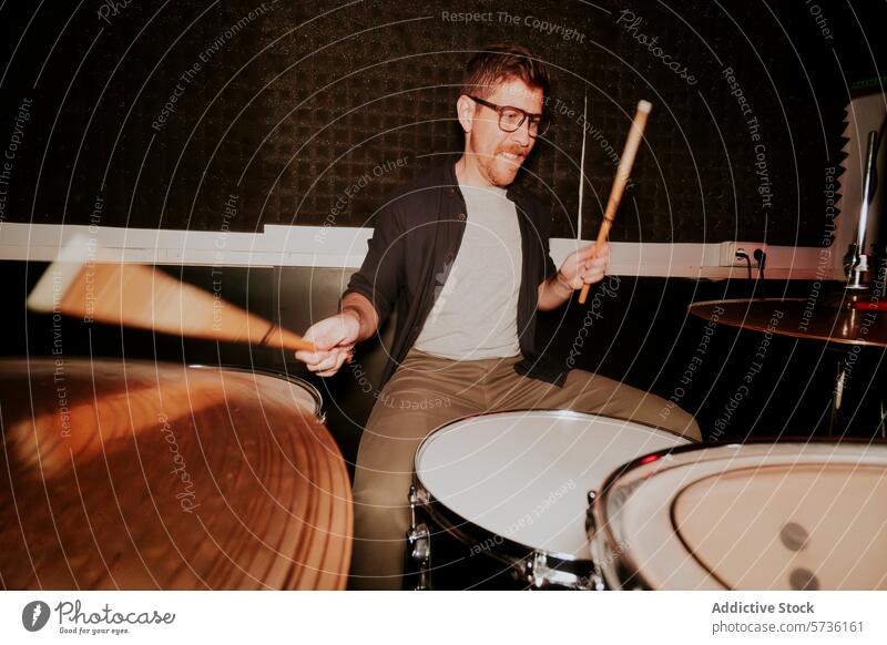 Dynamic male drummer playing in a dimly lit room man music band instrument glasses smile energetic performance motion entertainment sticks beat rhythm dark