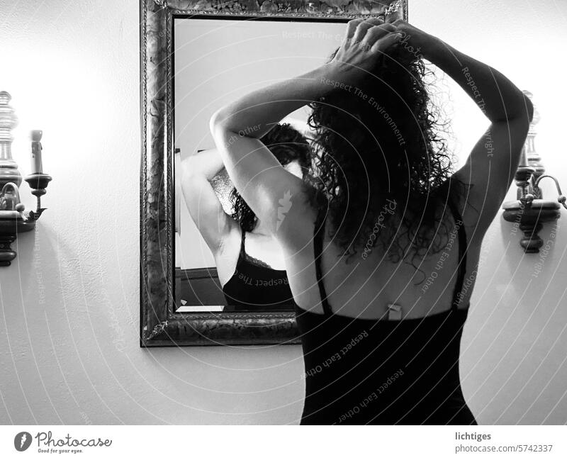 Back mirror- Young woman straightens her hair in the mirror Mirror Mirror image back view black-and-white Evening