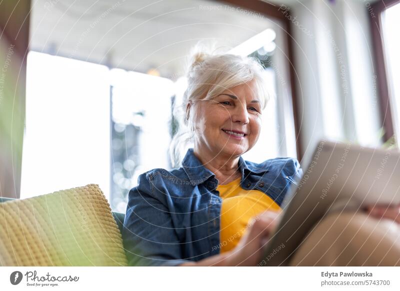 Mature woman using digital tablet while sitting on sofa at home people casual day portrait indoors real people white people adult mature retired old one person