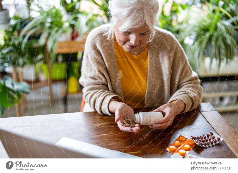 Senior woman taking pills from a bottle while sitting at the table at home people casual day portrait indoors real people white people adult mature retired old