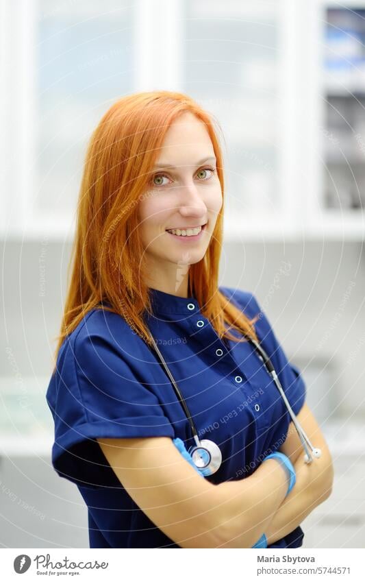 Vertical portrait of beautiful redhead female doctor during appointment of patient in office a modern clinic. Skillful woman veterinarian is at the workplace in vet hospital.