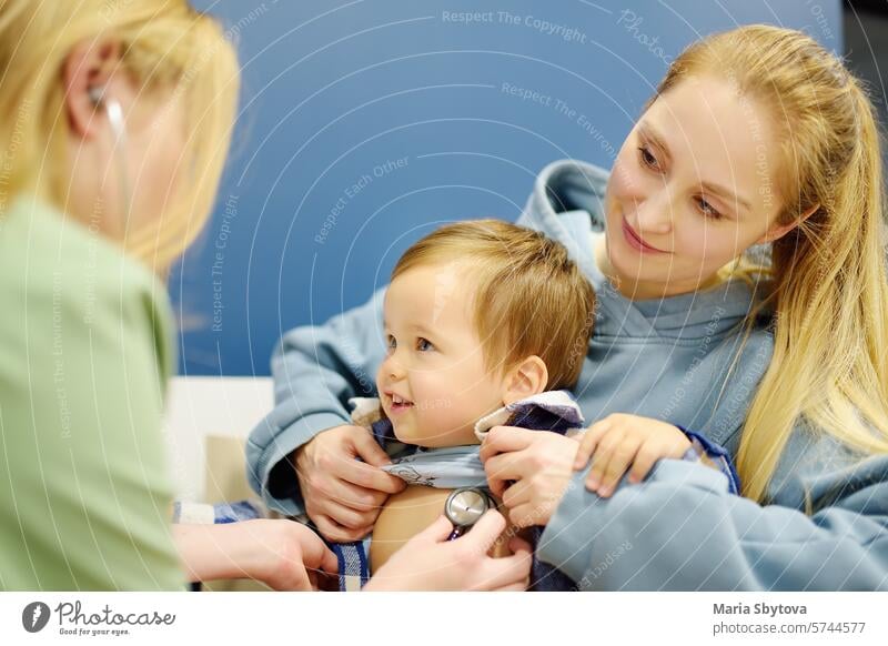 A cute toddler boy is at an appointment with a caring pediatrician. The doctor is listening to heartbeat and breathing of a little patient using stethoscope