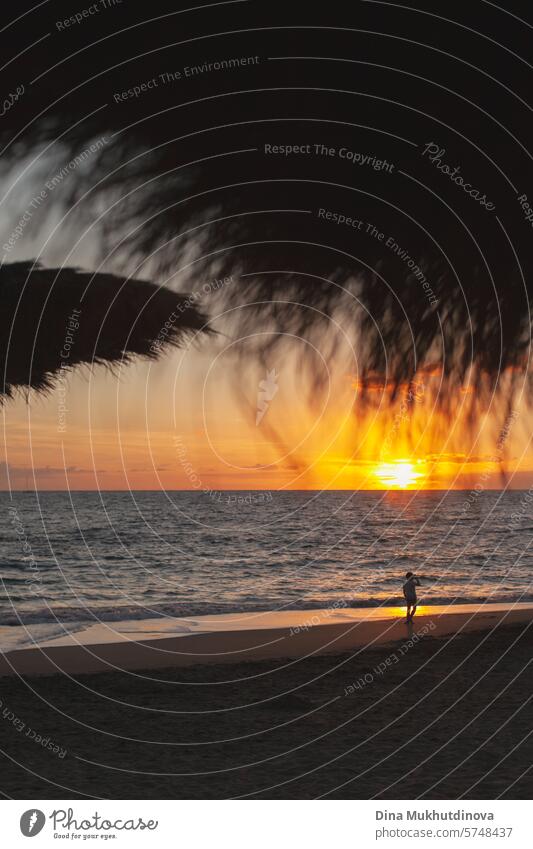 sunset at the ocean. Beach vacation. Vertical shot. beach umbrellas silhouette. Distant silhouette of a person walking on the beach. Vacation & Travel Sunset