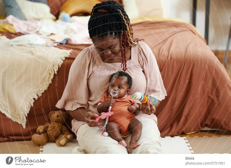 Black woman sitting on floor and playing with baby girl sucking pacifier toy mother kid soother leisure newborn Baby motherhood little sleep calm give child