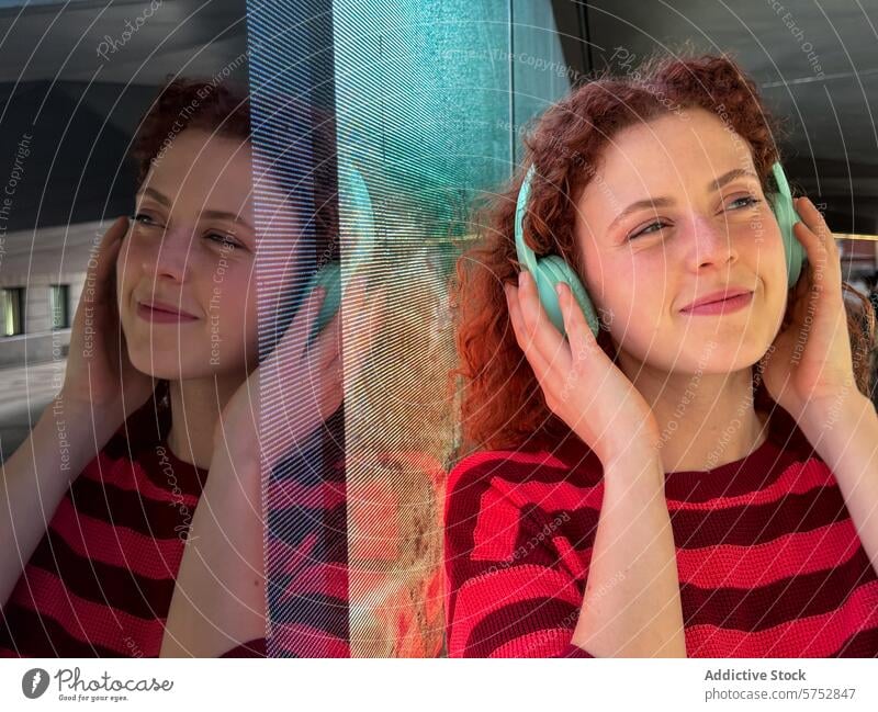 Young redhead woman enjoying music with headphones outdoors young smiling curly hair red hair reflection glass teal striped shirt enjoyment leisure listening