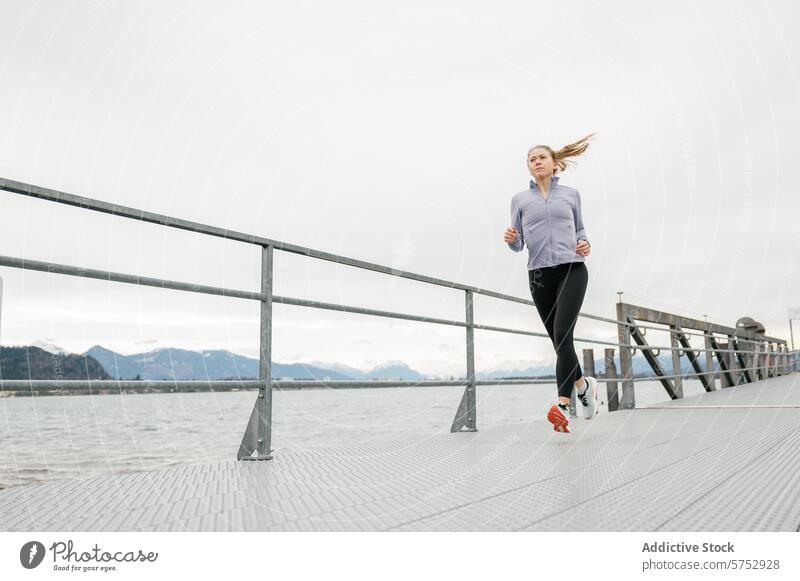 Young woman jogging along a serene waterfront athlete run boardwalk tranquil bay mountain backdrop young outdoor exercise fitness active lifestyle health