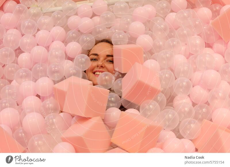 Young female smiling in ball pit with pink background woman twenties blue eyes portrait feminist authentic people beauty diverse pretty cute ballpit balls