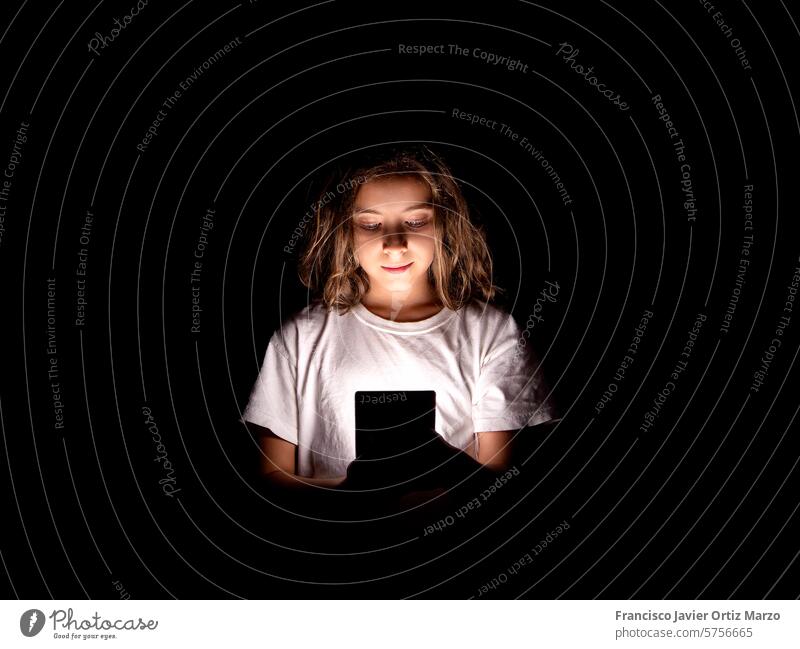 Young Girl Engrossed in Smartphone, Illuminated in Darkness girl young smartphone darkness internet social media danger online child screen time night light