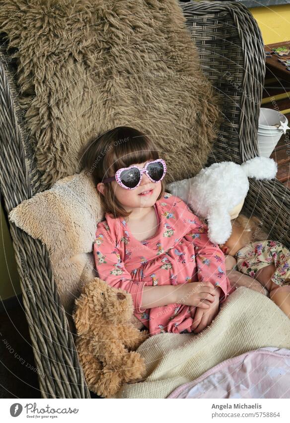 Toddler sitting in an armchair with sunglasses on the balcony and a cuddly toy next to him Toddler with sunglasses Armchair with lambskin Summer Sun reflection