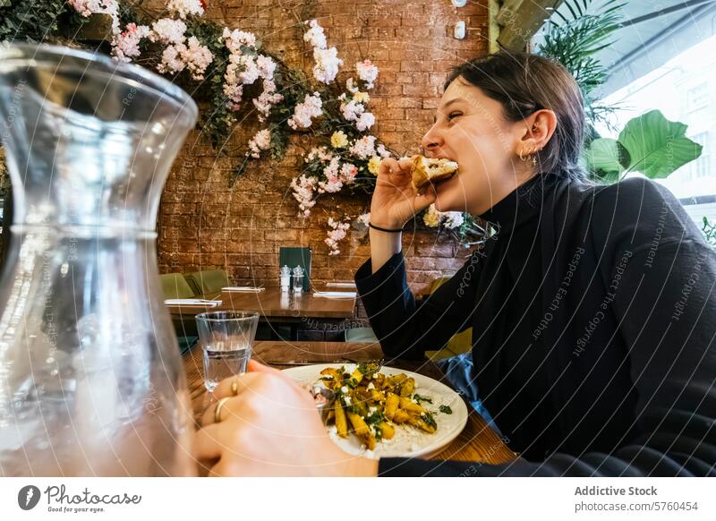 Caught in a moment of delight, a woman bites into a sandwich, surrounded by an inviting cafe atmosphere with vibrant floral wall decor eating plate enjoyment