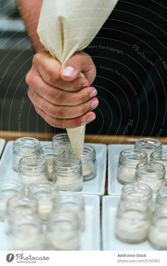 Close-up of anonymous chef's hands as they skillfully pipe vanilla cream into small glass jars, preparing a gourmet dessert piping preparation pastry filling