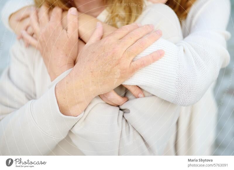 Cute woman tenderly hugs her mature mother on Mother's Day. Close up view of hands. Mothers day mom mama adult child embrace daughter parent friends outside