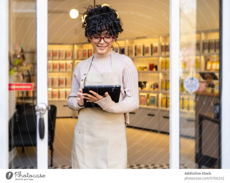 Smiling hispanic woman business owner with tablet in storefront entrepreneur digital device boutique smiling cheerful apron entrance shop retail door welcome