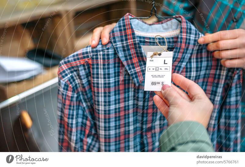Close up of unrecognizable woman client hand holding label of plaid shirt on clothing shop customer shopping clothes apparel store female looking tartan hanger