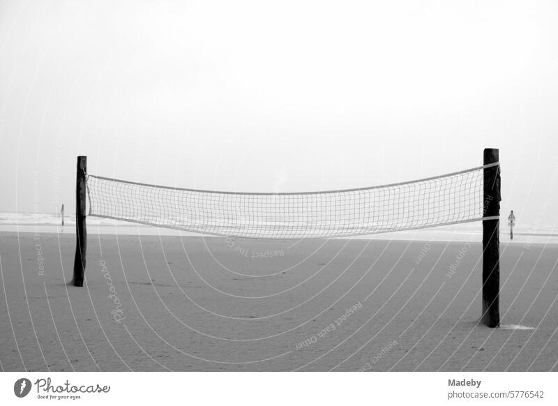 Volleyball net for beach volleyball in the rain and storm at the beach playground on the beach of St. Peter-Ording in the district of Nordfriesland in Schleswig-Holstein in the fall on the North Sea coast in neo-realistic black and white