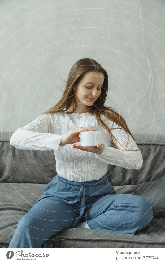 Young woman on couch holding cream jar in hands skin care beauty applying young moisturizer female treatment cosmetics girl spa moisturizing healthy closeup