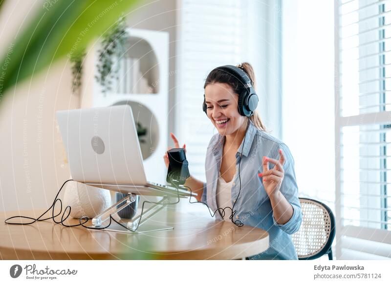 Woman wearing headphones sitting at a desk speaking into microphone and recording a podcast woman people one person room living room adult young young adult