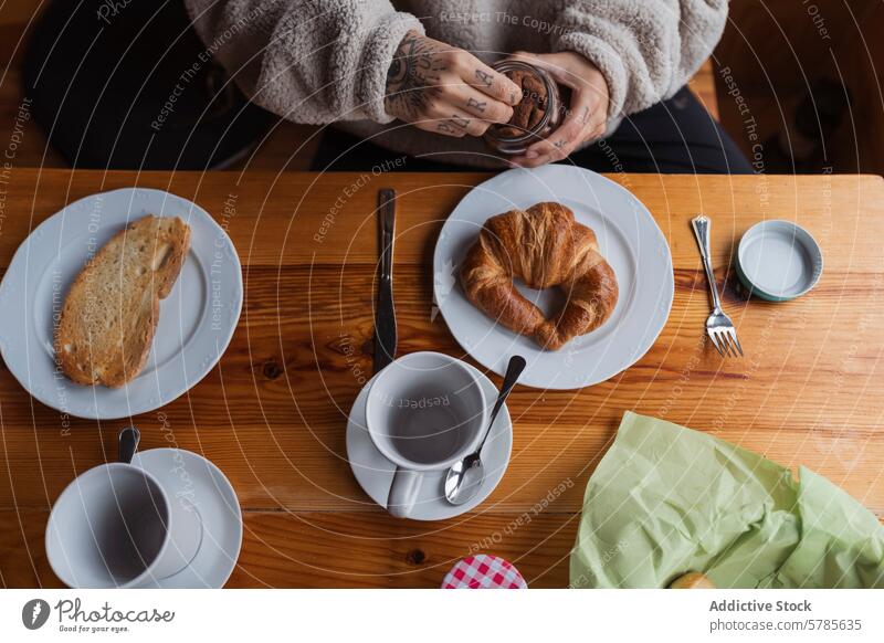 Cozy breakfast table with fresh pastry and tattooed hands croissant coffee cup plate wood bread fork knife cozy morning meal modern style lifestyle hipster ink
