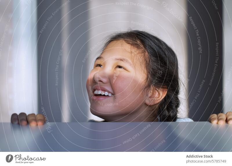 Young girl's cheerful smile in gentle lighting happy joy childhood young peeking peering surface innocence teeth bathed soft bright indoor cute laughter emotion