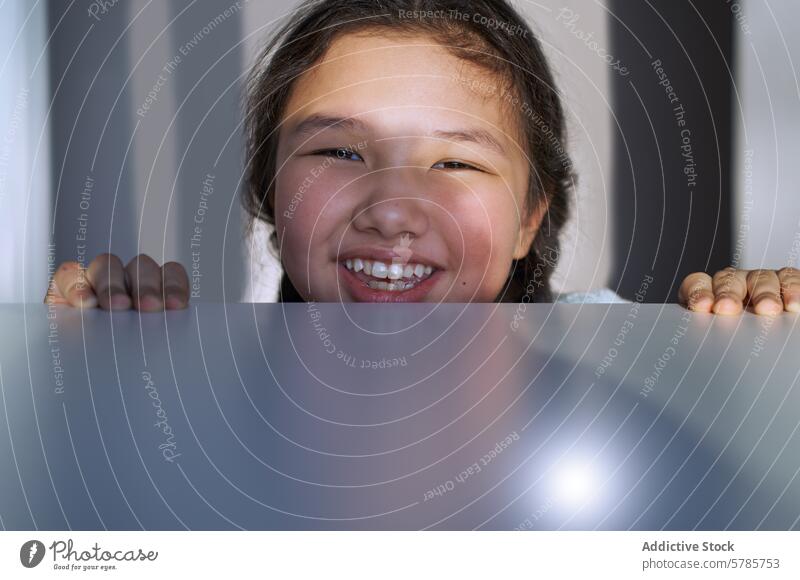 Smiling young girl peeking over a glossy surface smile close-up cheerful youth happy expression positivity child teeth blurred joy indoor person playful