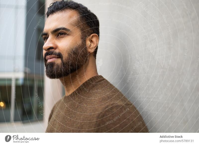 A contemplative man gazes into the distance, his profile captured against the minimalist background of an urban setting pensive thoughtful bearded sweater