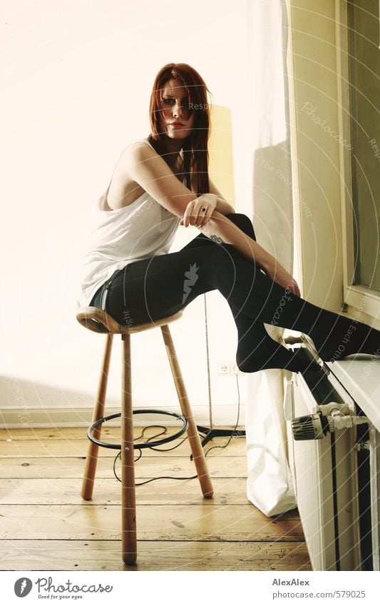 Young woman sitting on a stool by the radiator Youth (Young adults) Arm Legs 18 - 30 years Adults Shirt Tights Red-haired Long-haired Floorboards Heating Window