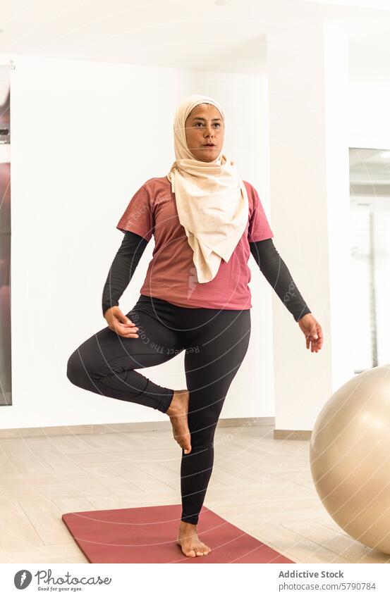 Muslim woman practicing Vrksasana yoga pose in locker room muslim vrksasana tree pose exercise hijab preparation fitness balance focus wellness health