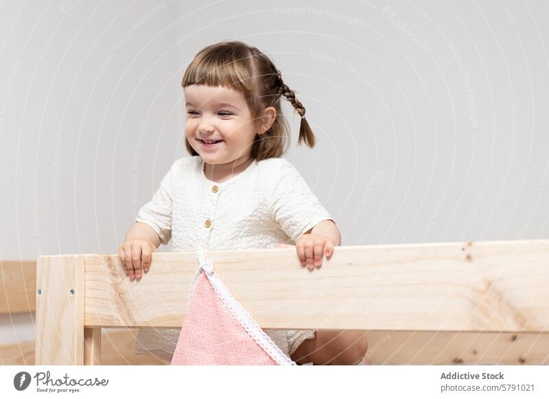 Smiling Toddler Girl Leaning on Wooden Furniture toddler girl smiling happy wood furniture innocence joy child braid hair lean structure playful cute indoor
