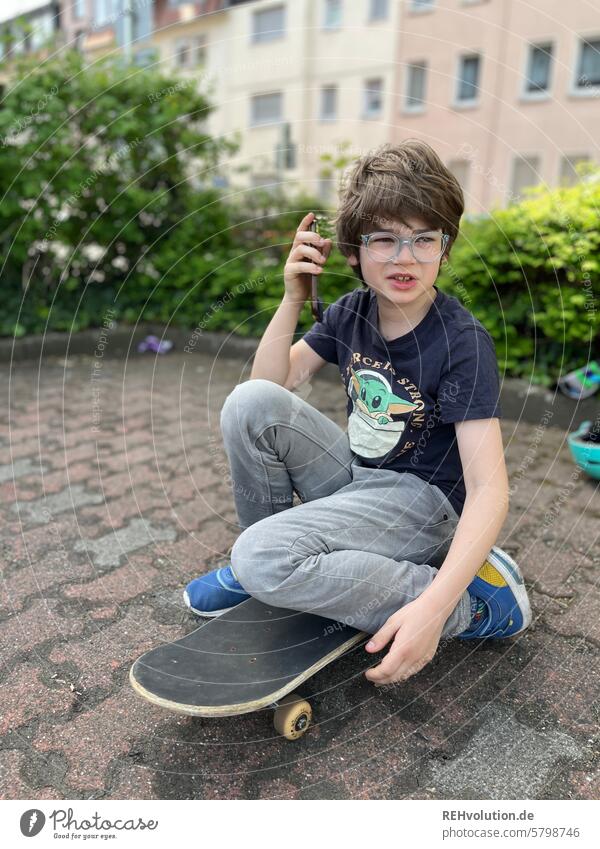 Boy sitting on a skateboard and talking on his cell phone Child Infancy Boy (child) naturally Authentic fun Exterior shot Future Brash Looking urban Town