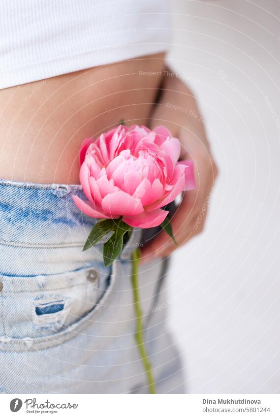 pink peony in hand near skin and jeans on attractive young woman, style fashion and lifestyle, female intimate healthcare flower symbol beautiful bouquet adult