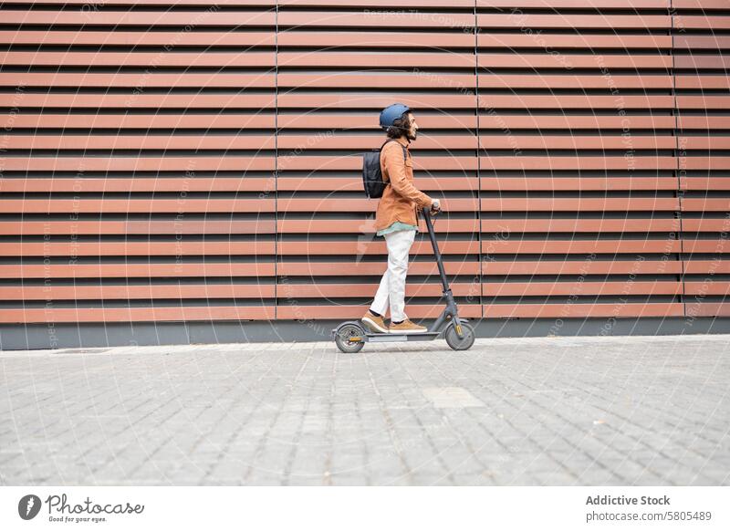 Urban lifestyle: young man riding an electric scooter urban eco-friendly transport beard helmet blue modern striped background outdoor mobility sidewalk