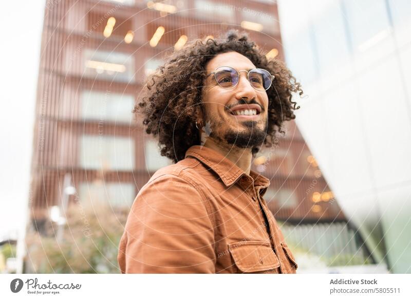 Smiling man riding an electric scooter in the city urban modern building joyful curly hair happy freedom transportation mobility eco-friendly young adult