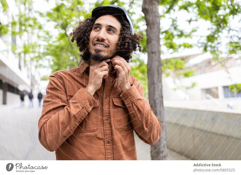 Young man adjusting helmet outdoors before urban ride safety responsible enjoyment curly hair young adult male city transportation eco-friendly mobility