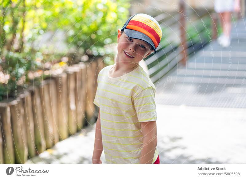 Young boy in colorful cap smiling outdoors smile striped yellow t-shirt cheerful summer park nature child young happy sunlight day casual fashion leisure