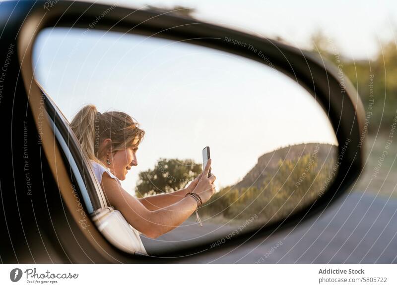 Woman capturing the landscape on her phone through car mirror woman smartphone side mirror reflection outdoor scenic photo photography technology travel leisure