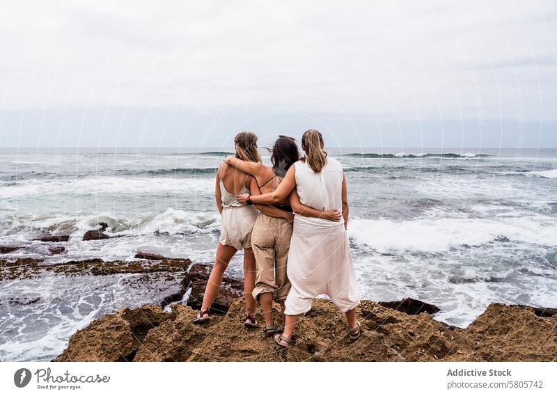 Friends embracing by the ocean on a cloudy day friendship women embrace rocky shore sea wave sky unity togetherness coast outdoor nature landscape tranquility