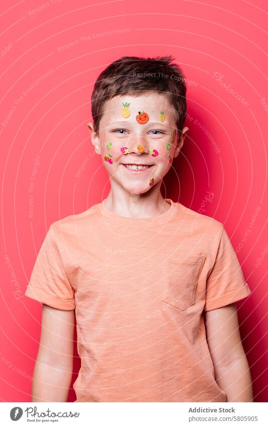 Happy schoolboy with face stickers smiling at camera smile look direct pink background joy happy colorful fruit celebrate decoration childhood fun cheerful