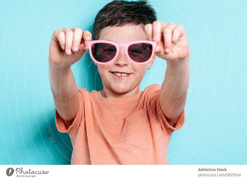 Smiling School Boy with Pink Sunglasses school kid boy smile playful sunglasses pink blue background happiness childhood eyewear fashion style cheerful