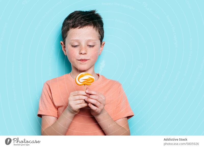 Young boy admiring a lollipop on blue background school kid treat snack sweet candy looking down serene contemplating child caucasian delight enjoyment leisure