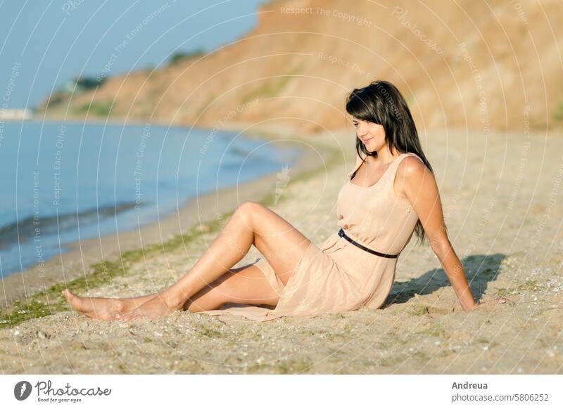 girl with black hair in a beige dress on the shore of the ocean white go seas background horizon surf water blue sunny day summer warmth flower walk sand