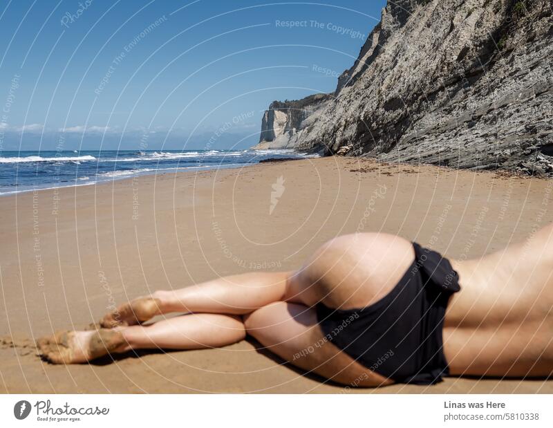 Such a beautiful beach in Corfu, Greece. Accompanied by a topless girl who is lured by the sun. A pretty woman sunbathing on such a picturesque coast. Surrounded by mountains, rocks, and golden sand.