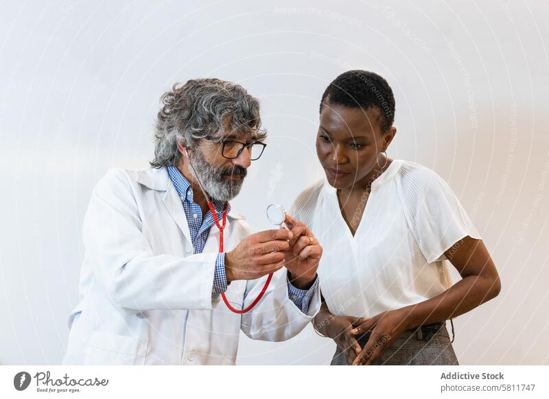 Elderly doctor showing stethoscope to patient check up appointment examine hospital health care visit multiethnic multiracial diverse black african american