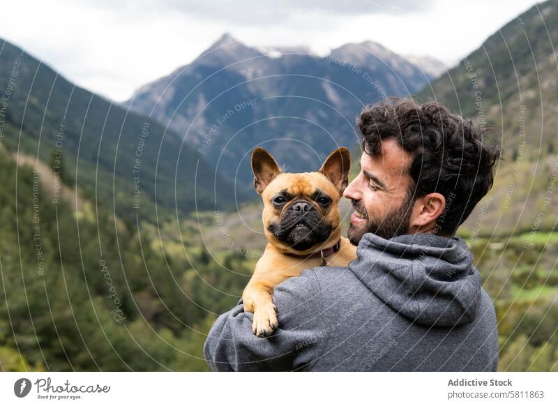 Happy traveling man embracing cute dog in highlands mountain kiss together embrace traveler hiker male pyrenees french bulldog rock freedom pet animal journey