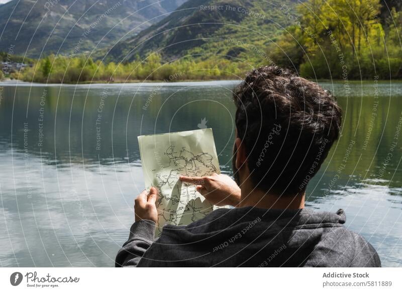 Traveling man reading map near lake in highlands traveler navigate orientate mountain search male pyrenees trip route journey explore direction vacation