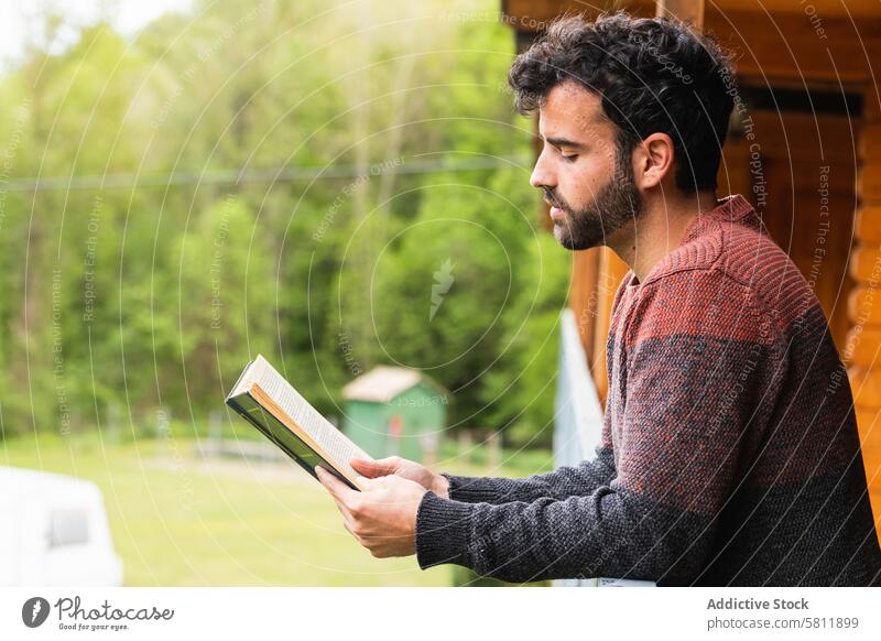 Thoughtful man reading book on terrace of house literature interesting hobby thoughtful novel male pyrenees wooden calm story relax concentrate lean railing