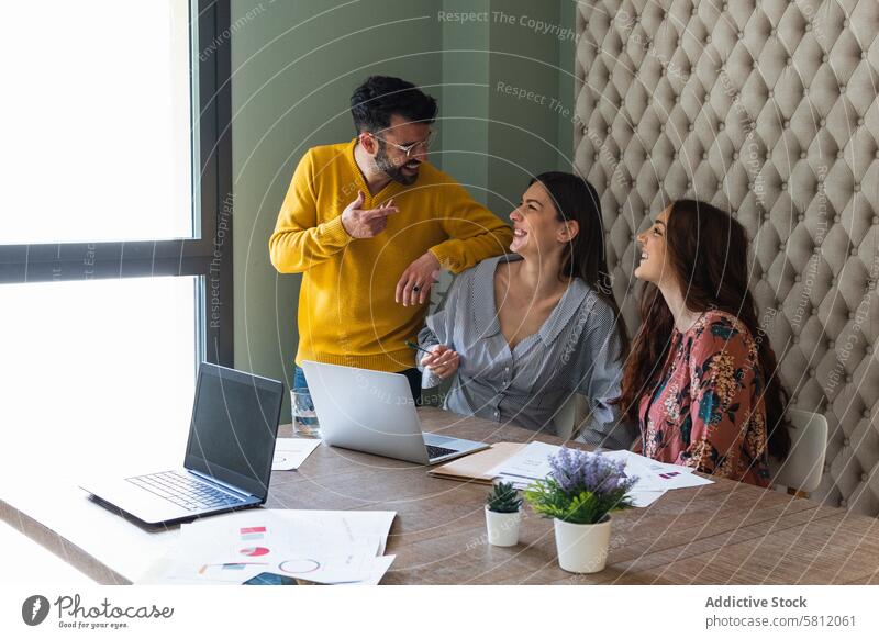 Joyful colleagues discussing project in modern workspace cheerful office group laugh teamwork coworker communicate workplace document toothy smile business