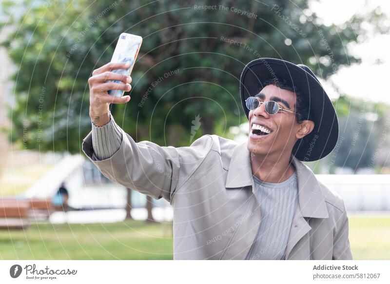 Stylish ethnic man taking selfie on smartphone trendy style using happy hipster positive cool male smile self portrait stand optimist building outerwear